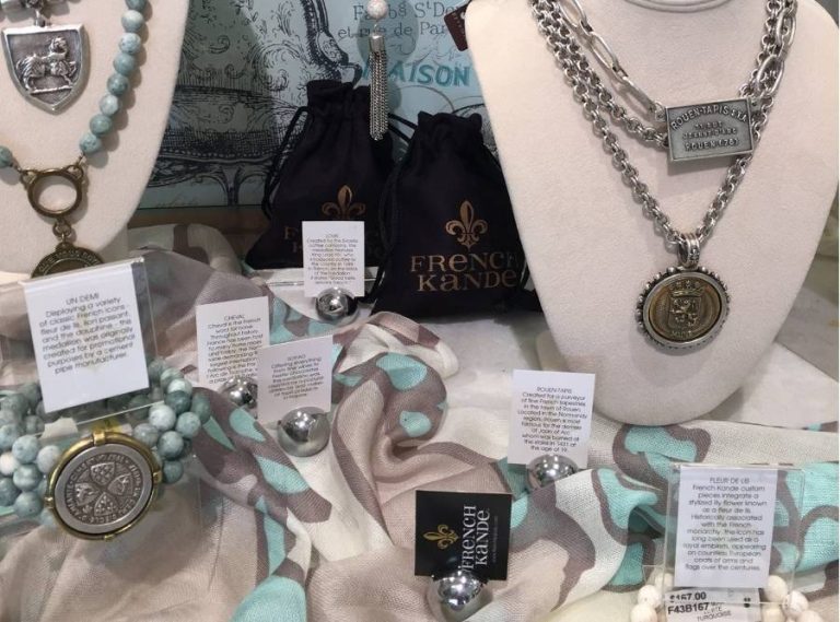 French Kande designer jewelry display with silver medallion necklaces, beaded bracelets, and branded packaging